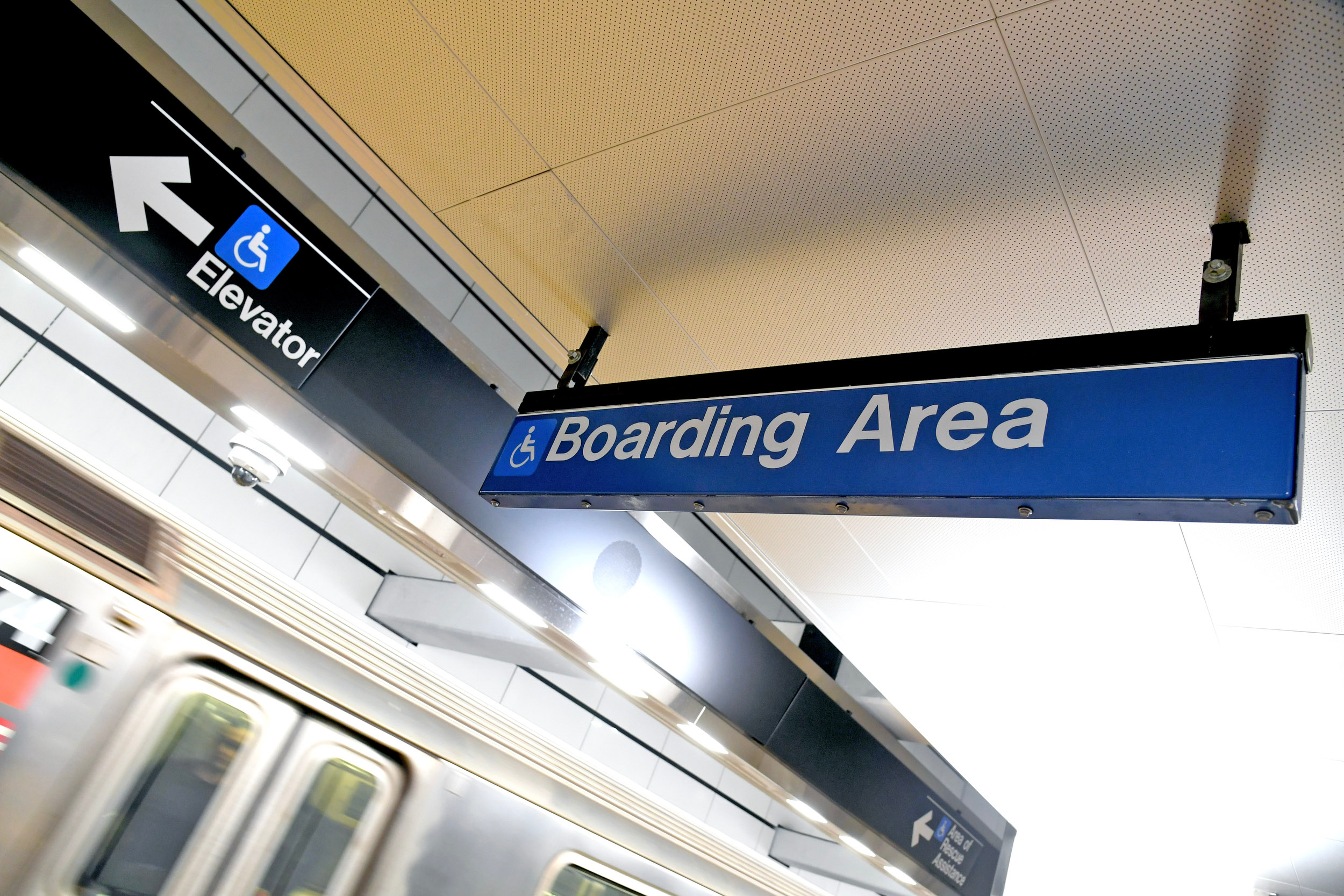 A blue sign with the words "Boarding area" and an icon showing a person in a wheelchair. On a different sign on the left is the same icon and an arrow pointing toward elevators.