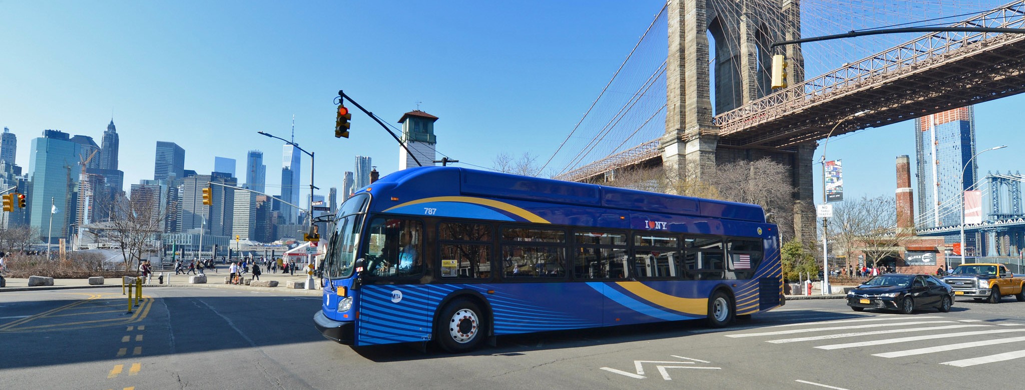 A bus on the Brooklyn waterfront in front of the Manhattan skyline. 