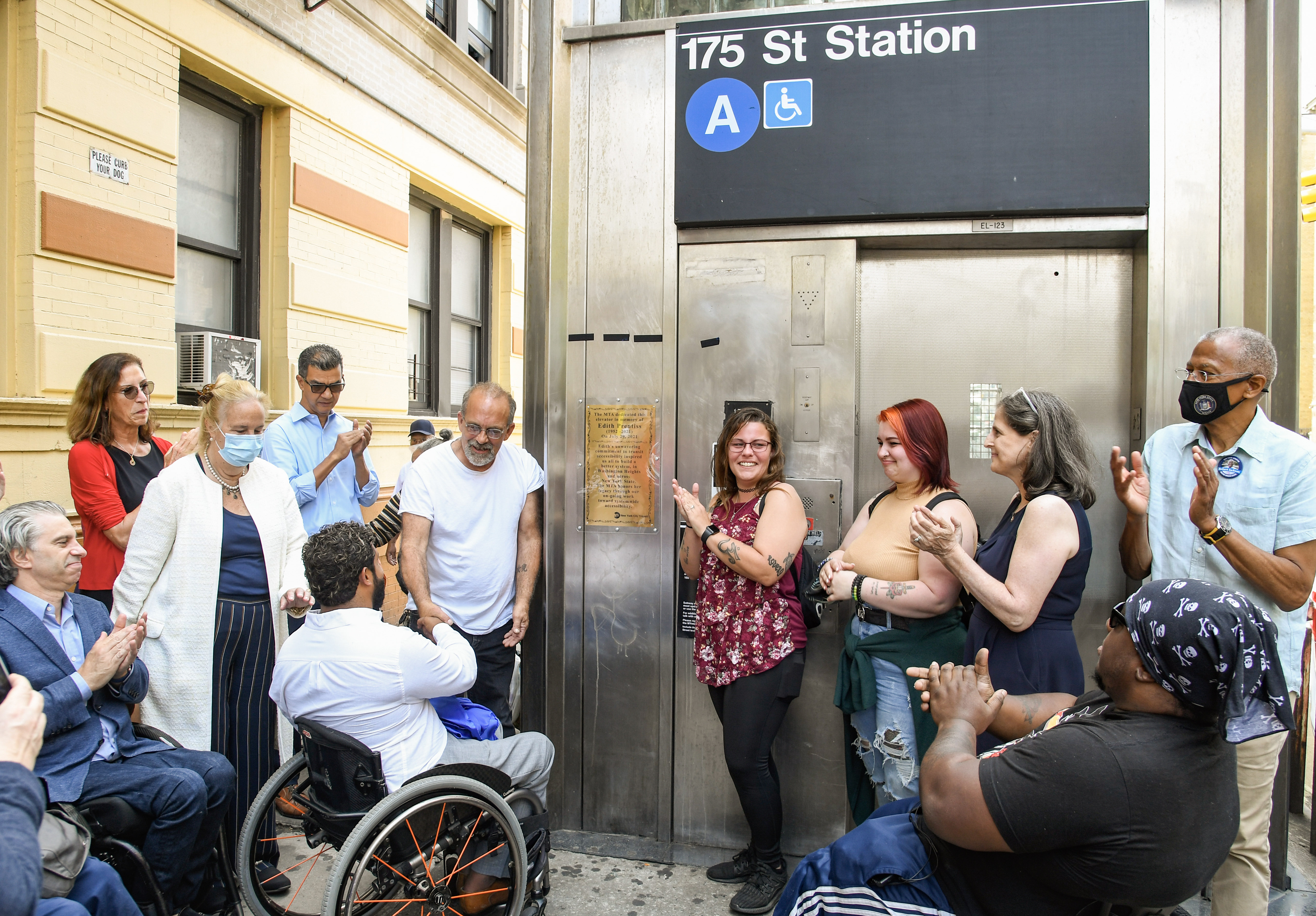 Chief Accessibility Officer Quemuel Arroyo and advocates stand around 175 Street elevator clapping as a plaque is revealed.