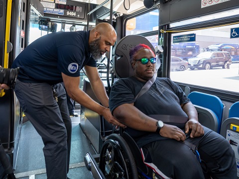 A bus operator assisting a customer in a mobility device with their seatbelt using the Quantum self-securement system.