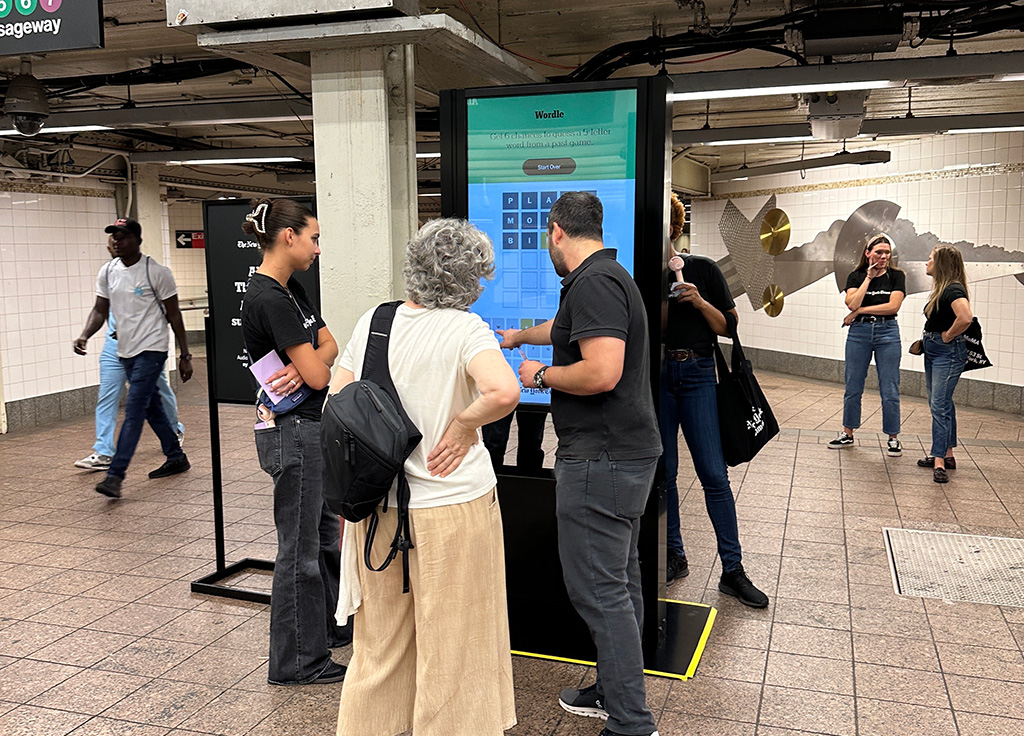 An interactive Wordle game on a digital screen at a subway station