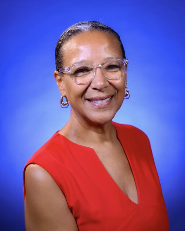 A woman wearing a red shirt and glasses. Her hair is pulled back in a ponytail and she is smiling.