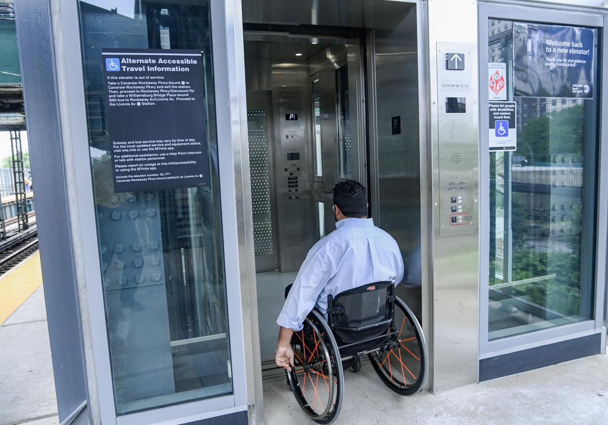A man using a wheelchair enters an elevator on a subway platform. 