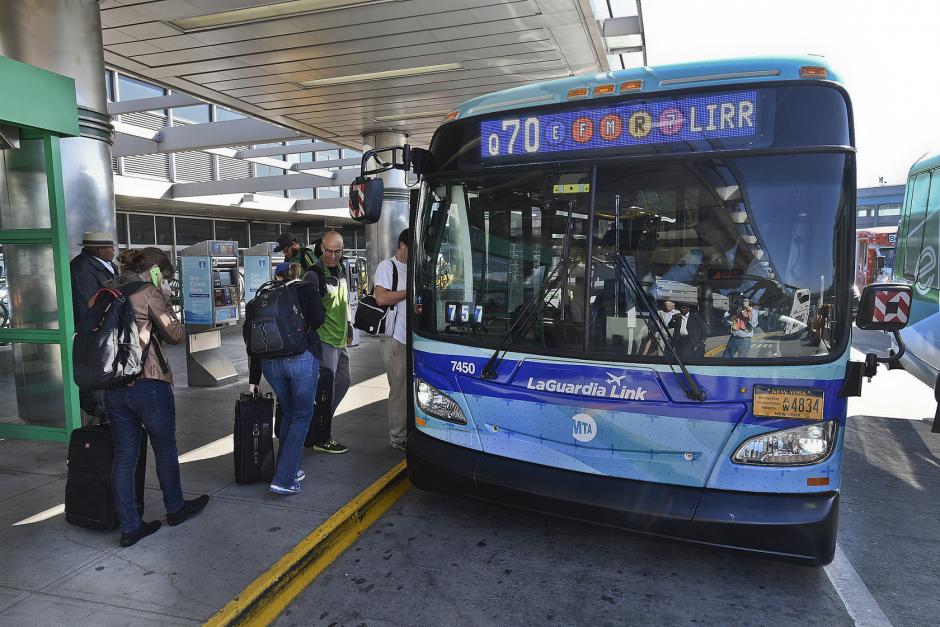People with luggage wait in line to board a blue Q70 bus with a "LaGuardia Link" decal on the front.