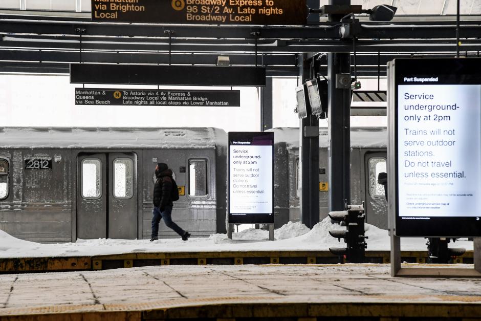 A person walks on a snowy outdoor subway platform. Digital screens say service will be underground-only starting at 2 p.m.